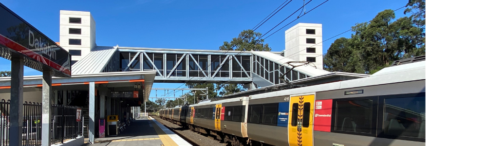 Photograph of upgraded Daklabin station showing platform 1 with new station building, footbridge, lifts and a train arriving