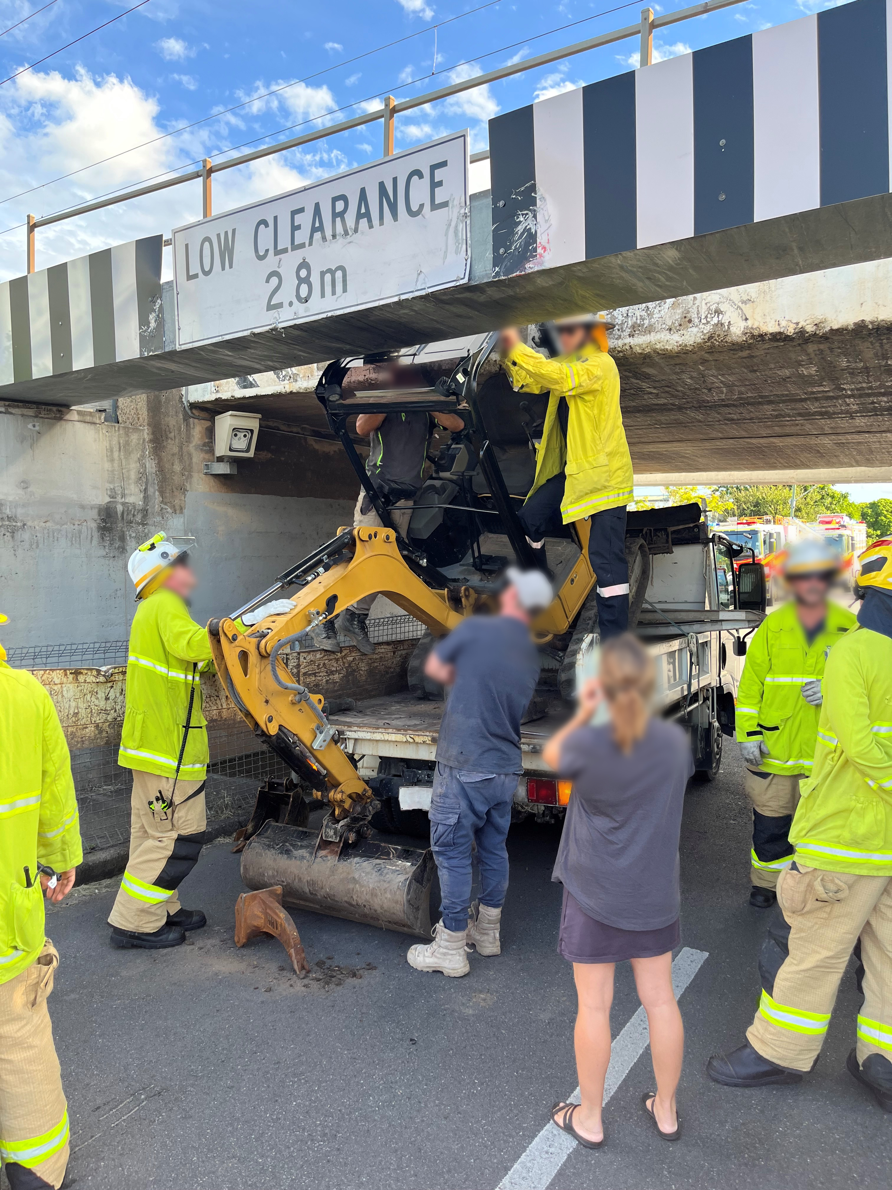 Firefighters cutting the top off an excavator stuck under a rail bridge