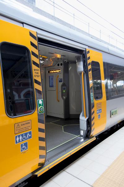 Train at station with doors open. Shows door open button, yellow safety handles and the gap between platform and train. 