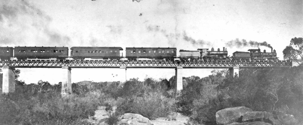 A black and white photograph of the Sydney Mail train crossing Quart Pot creek rail bridge a heritage-listed railway bridge at Quart Pot Creek, Stanthorpe in the Southern Downs Region of Queensland, full image description is available below.
