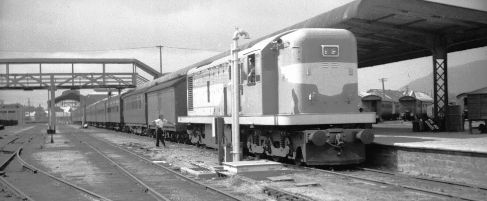 A black and white photograph of a 1150 class diesel electric locomotive at Rockhampton railway station, full image description is available below.