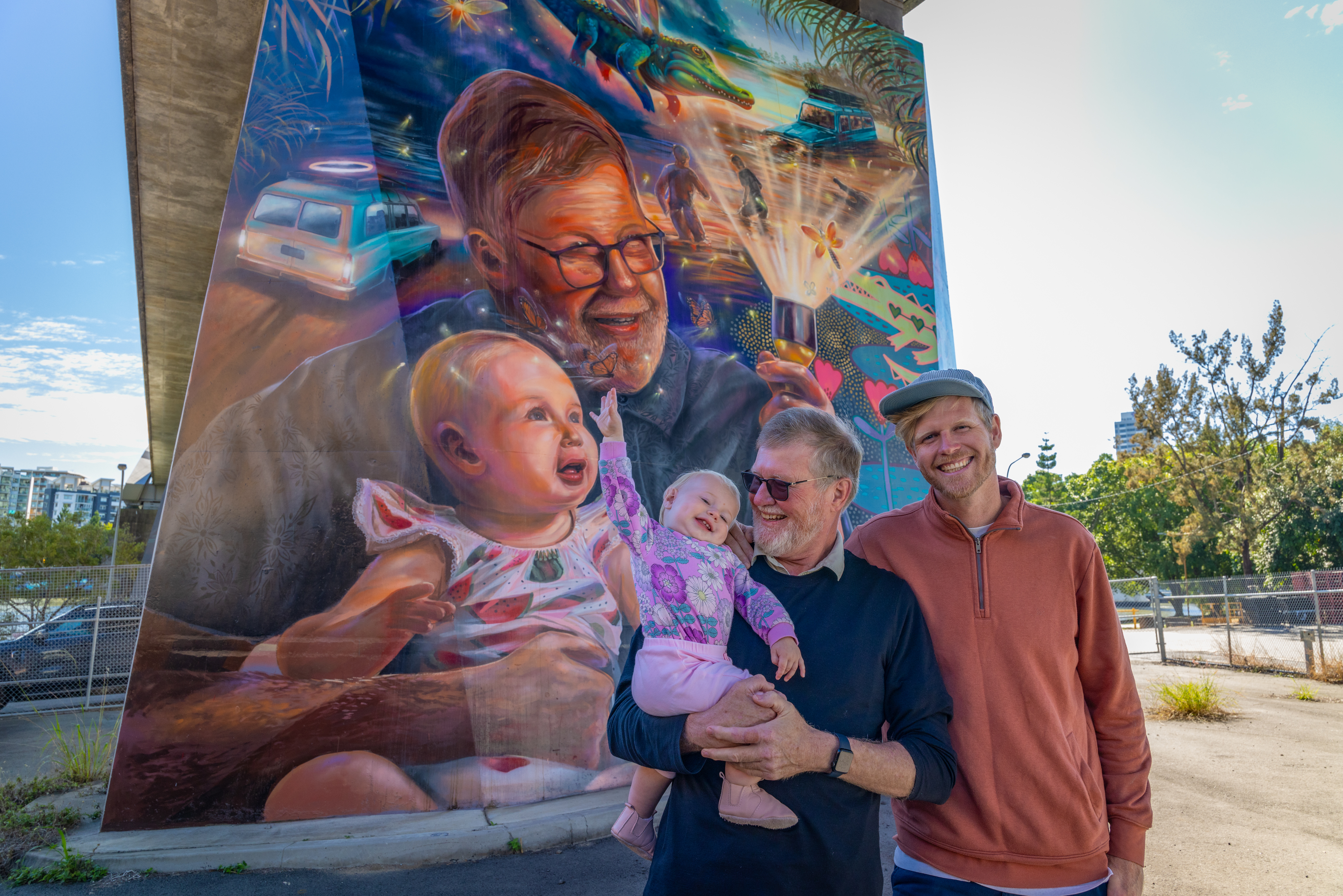 Artist Joel Fergie in front of his artwork, standing with his father and his daughter.